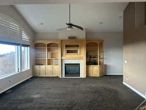 Unfurnished living room with a ceiling fan, a fireplace, and dark colored carpet