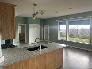 Kitchen with light stone countertops, pendant lighting, a peninsula, brown cabinetry, and dark wood finished floors