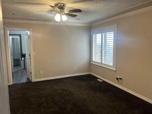 Spare room with ornamental molding, dark colored carpet, and ceiling fan