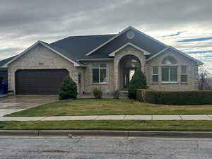 View of front facade with brick siding, a front yard, driveway, and an attached garage