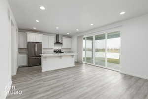 Kitchen with a kitchen island with sink, white cabinetry, recessed lighting, freestanding refrigerator, and light wood-type flooring