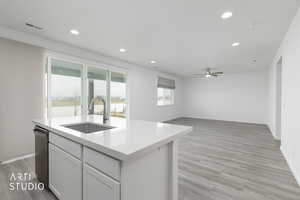 Kitchen with white cabinets, light wood-style floors, light stone counters, an island with sink, and recessed lighting