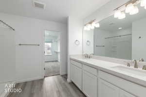 Bathroom with double vanity, a shower, and light wood-type flooring