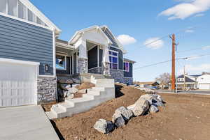 View of front of home featuring stone siding, a garage, and covered porch
