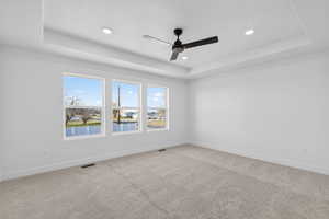 Carpeted spare room with a raised ceiling, a water view, a ceiling fan, and recessed lighting