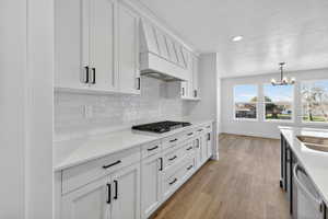 Kitchen featuring tasteful backsplash, white cabinetry, pendant lighting, a textured ceiling, and light stone counters