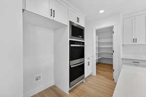 Kitchen featuring backsplash, stainless steel appliances, white cabinetry, light wood-style floors, and recessed lighting