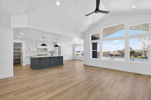 Unfurnished living room with light wood finished floors, recessed lighting, a chandelier, ceiling fan, and high vaulted ceiling