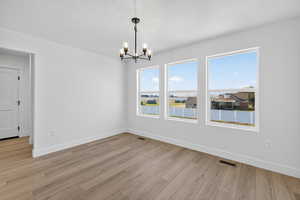 Unfurnished dining area featuring light wood-style flooring, a chandelier, and a textured ceiling