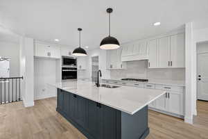 Kitchen with white cabinetry, a kitchen island with sink, appliances with stainless steel finishes, tasteful backsplash, and light wood-style floors