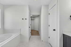 Bathroom featuring a bath, light marble finish flooring, a spacious closet, and vanity