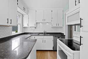 Kitchen with white appliances, white cabinets, tasteful backsplash, dark stone countertops, and light wood finished floors