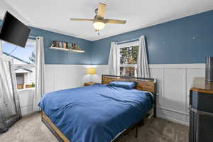 Carpeted bedroom featuring a wainscoted wall, a decorative wall, and a ceiling fan