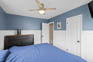 Bedroom with a wainscoted wall, ceiling fan, and a decorative wall