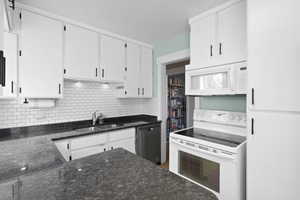 Kitchen with white appliances, decorative backsplash, white cabinets, and dark stone counters