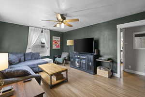Living room featuring wood finished floors, a textured wall, ceiling fan, and a textured ceiling