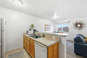 Kitchen with a peninsula, open floor plan, light countertops, white appliances, and brown cabinetry