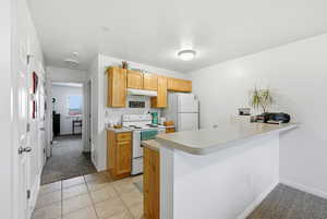 Kitchen with light colored carpet, white appliances, light tile patterned floors, light countertops, and under cabinet range hood