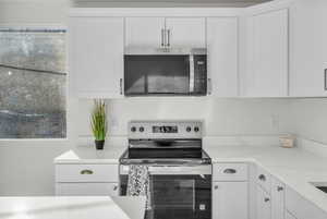 Kitchen with stainless steel appliances, white cabinets, and light stone counters