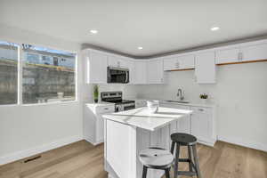 Kitchen with white cabinetry, stainless steel appliances, a kitchen breakfast bar, light wood-type flooring, and a center island