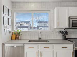 Kitchen with stainless steel appliances, white cabinetry, light countertops, and decorative backsplash