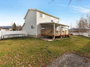 Rear view of property with a fenced backyard, a trampoline, and a deck