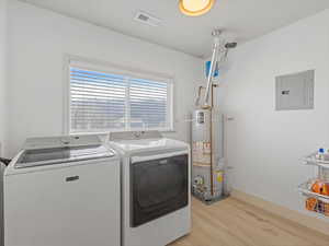 Laundry room featuring electric panel, washing machine and dryer, water heater, and light wood-style flooring
