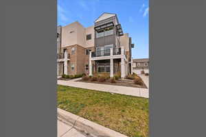 View of front of house featuring stucco siding, a front lawn, a balcony, and brick siding