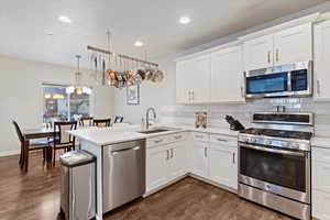 Kitchen featuring appliances with stainless steel finishes, white cabinetry, recessed lighting, backsplash, and decorative light fixtures