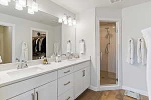 Master Full bathroom with a spacious closet, double vanity, a shower stall, dark wood-style floors, and baseboard heating