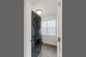 Laundry room with light tile patterned floors and stacked washer / dryer