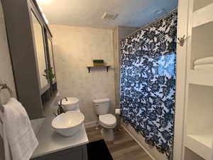Bathroom with wallpapered walls, a textured ceiling, vanity, shower / bathtub combination with curtain, and dark wood-style flooring