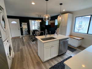 Kitchen featuring white cabinetry, stainless steel dishwasher, pendant lighting, a kitchen island with sink, and stacked washer / drying machine