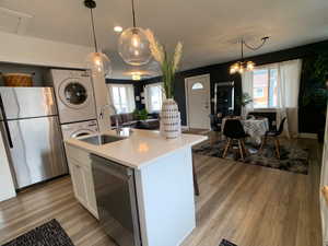 Kitchen featuring open floor plan, appliances with stainless steel finishes, white cabinetry, stacked washer / drying machine, and a kitchen island with sink