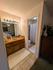 Ensuite bathroom featuring a ceiling fan, a shower with curtain, vanity, light tile patterned floors, and a textured ceiling