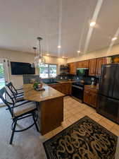 Kitchen featuring black appliances, a peninsula, dark stone countertops, a kitchen bar, and decorative light fixtures