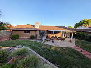 Rear view of house with a patio, a lawn, brick siding, and a chimney