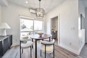 Dining room featuring a wall unit AC, light wood finished floors, and a chandelier