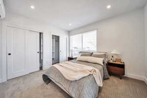 Carpeted bedroom with an AC wall unit, multiple closets, and recessed lighting