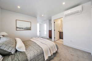 Bedroom featuring an AC wall unit, light carpet, connected bathroom, and recessed lighting