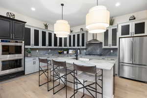 Kitchen featuring light stone countertops, stainless steel appliances, decorative light fixtures, a breakfast bar, and wall chimney range hood