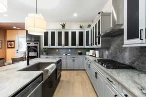 Kitchen with decorative light fixtures, light stone counters, wall chimney exhaust hood, light wood-type flooring, and recessed lighting