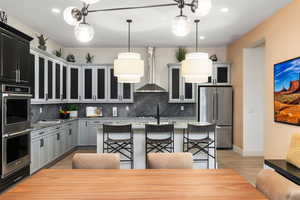 Kitchen with hanging light fixtures, appliances with stainless steel finishes, recessed lighting, wall chimney exhaust hood, and gray cabinets