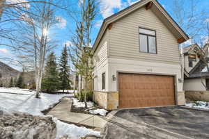 Snow covered property with stone siding, a garage, driveway, and stucco siding