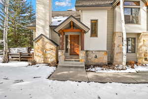 Snow covered property entrance featuring stone siding and a chimney