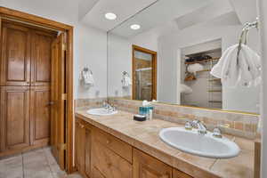 Full bath featuring a walk in closet, a shower stall, double vanity, light tile patterned flooring, and backsplash