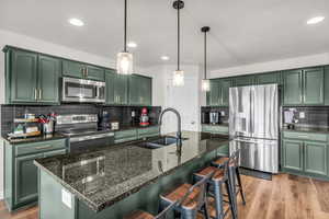 Kitchen with green cabinetry, appliances with stainless steel finishes, dark stone countertops, and recessed lighting