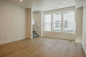 Unfurnished living room featuring light wood finished floors, stairs, and recessed lighting