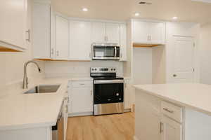 Kitchen with appliances with stainless steel finishes, white cabinets, light wood-style flooring, light stone counters, and recessed lighting