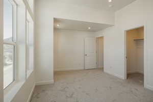 Unfurnished bedroom with light colored carpet, a spacious closet, and recessed lighting
